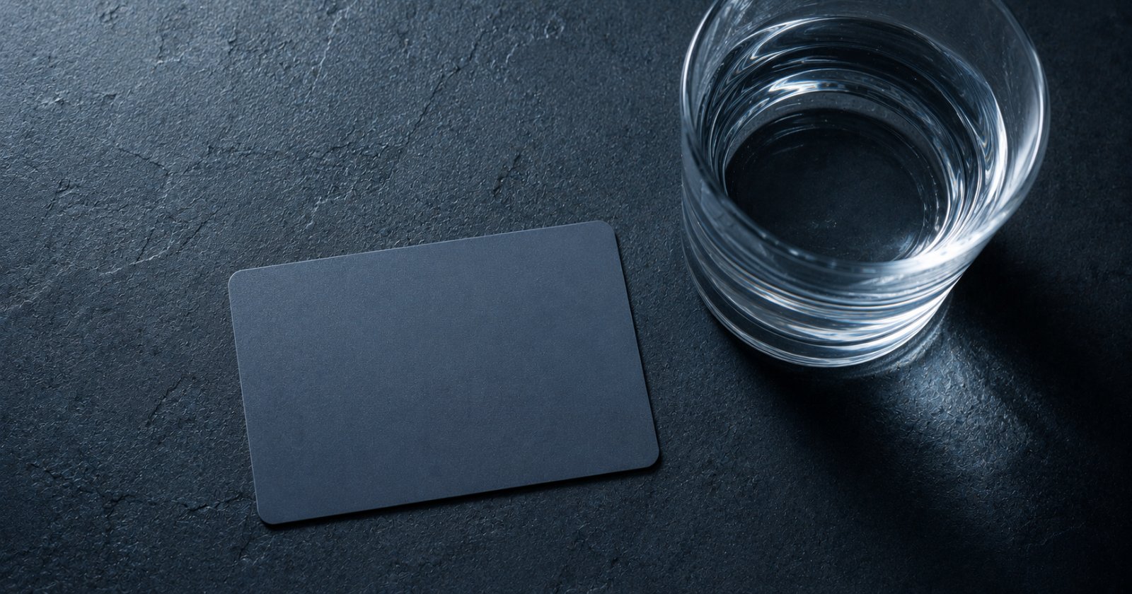 Tarjeta plástica sin marcas junto a un vaso de agua sobre una superficie oscura
